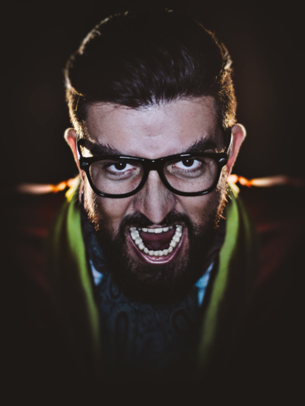Retrato de hombre con barba y gafas, expresión intensa y tatuajes visibles en el cuello.