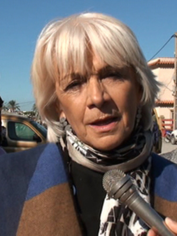 Entrevista en el exterior con una mujer hablando al micrófono, acompañada de otras personas.