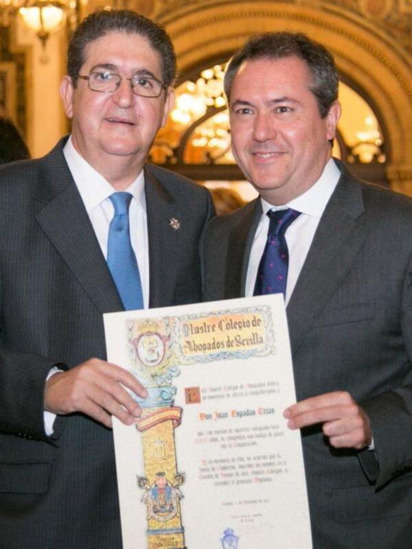 Dos hombres en trajes sostienen un diploma del Ilustre Colegio de Abogados de Sevilla.