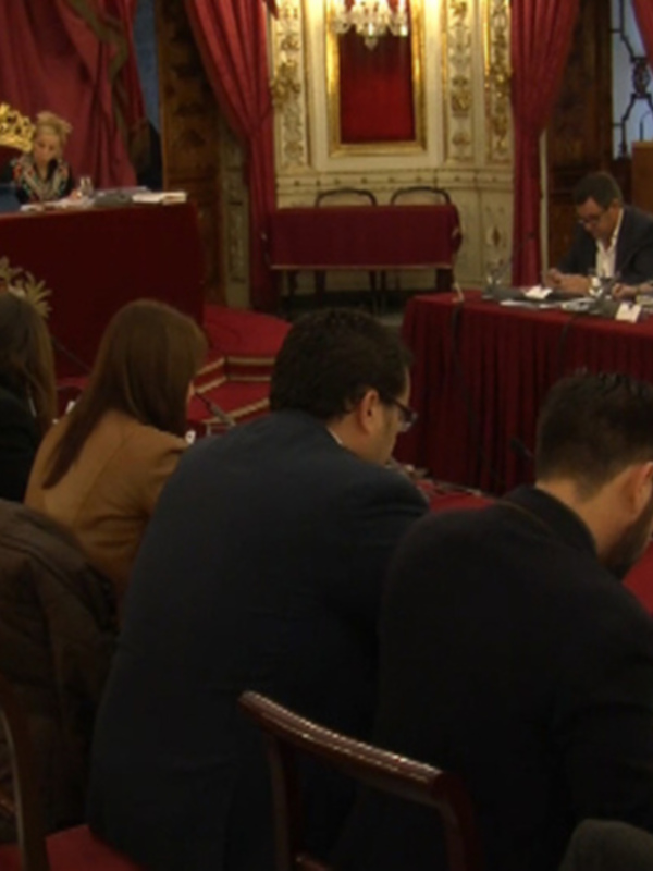 Reunión de trabajo en un salón formal con personas sentadas alrededor de una mesa.