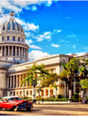 El Capitolio de La Habana, Cuba, bajo un cielo azul con nubes blancas, rodeado de coches clásicos y árboles.