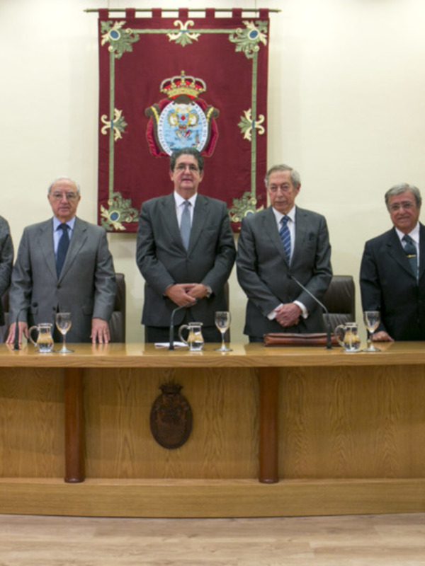 Oficiales en una reunión formal en un salón con banderas y un escudo de armas en el fondo.