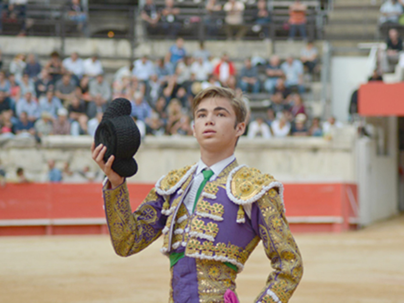 Joven torero saludando con el sombrero en el ruedo de una plaza de toros.