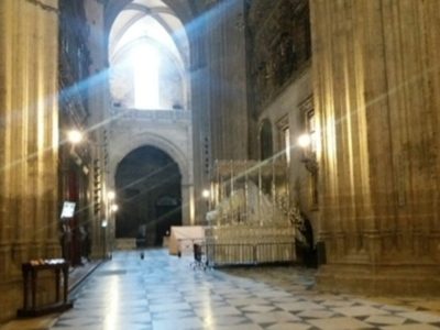 Interior de una catedral con arcos altos, columnas y luces que brillan desde el techo. La iluminación crea un efecto de luz que parece entrar por las ventanas altas, iluminando el suelo con patrones geométricos.