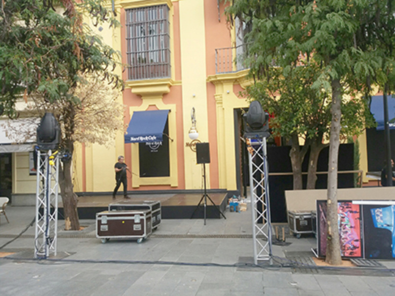 Escenario al aire libre con música en una plaza histórica, frente a un edificio amarillo con detalles arquitectónicos tradicionales.