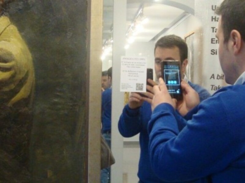 Un hombre toma una foto de un cuadro en un museo. El cuadro muestra a un hombre con barba y una chaqueta verde. En el fondo, hay una pared con información sobre la obra.