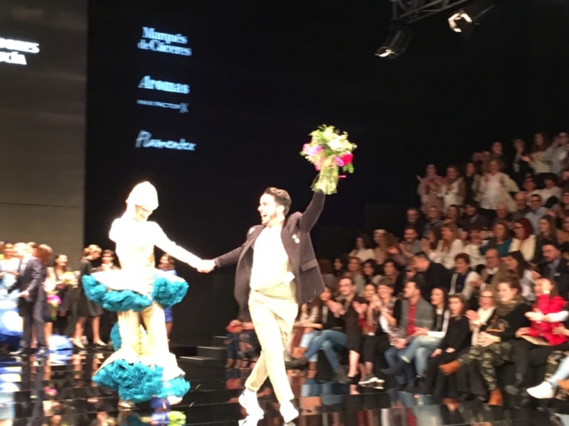 Modelos celebrando el final de la pasarela con flores en mano, mientras el público aplaude.