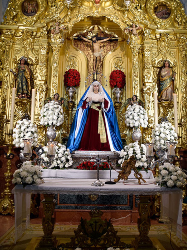Altar con estatuas religiosas y flores, decoración dorada y ornamentos en un entorno eclesiástico.
