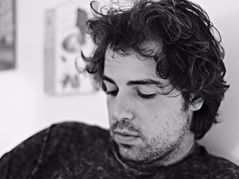 Retrato en blanco y negro de un hombre con cabello rizado y barba, mirando hacia abajo.