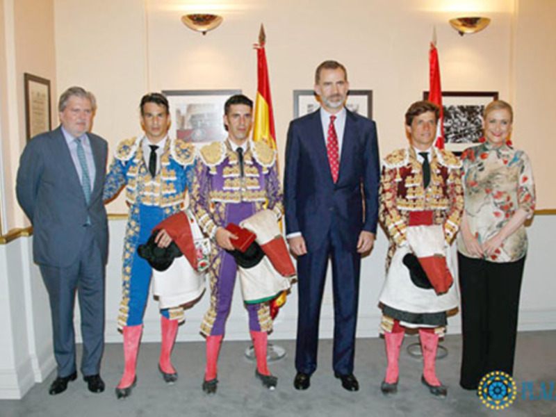 Grupo de personas en trajes formales y trajes de matador posando juntos en una sala decorada con banderas.