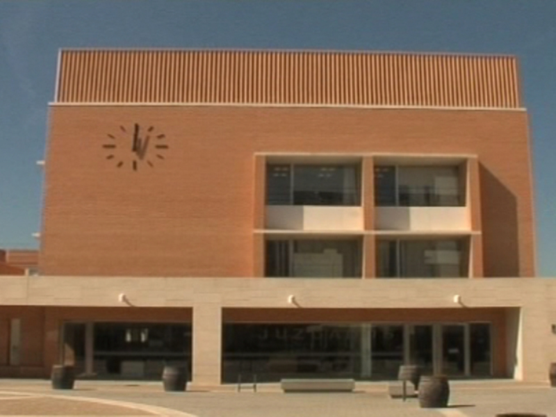 Edificio de oficinas con un reloj en la fachada, banderas y un patio abierto.