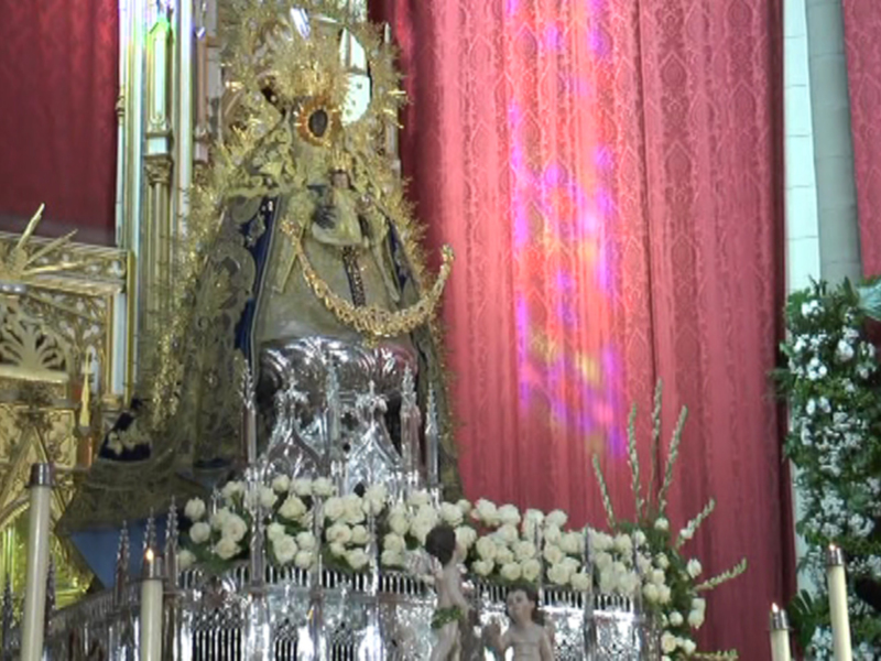 Imagen de la Virgen María en un altar con flores y decoración dorada, con luces de color rojo detrás.