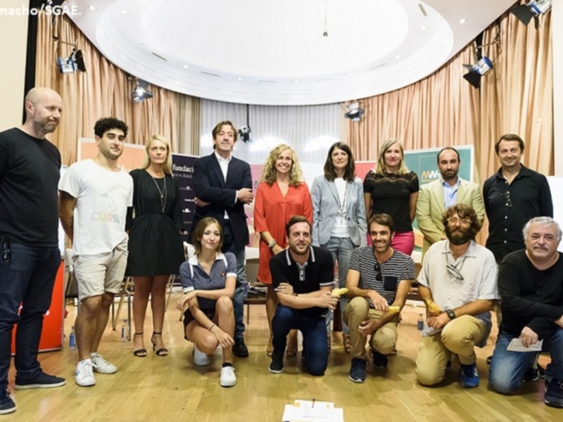 Grupo de personas posando para una foto en un evento formal en un salón circular con cortinas y luces de techo.