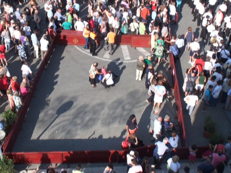 Una multitud de personas se reúne en un escenario rojo, con algunos individuos en el centro discutiendo. La imagen muestra una perspectiva aérea de la reunión, destacando el gran número de asistentes y su concentración en el escenario.