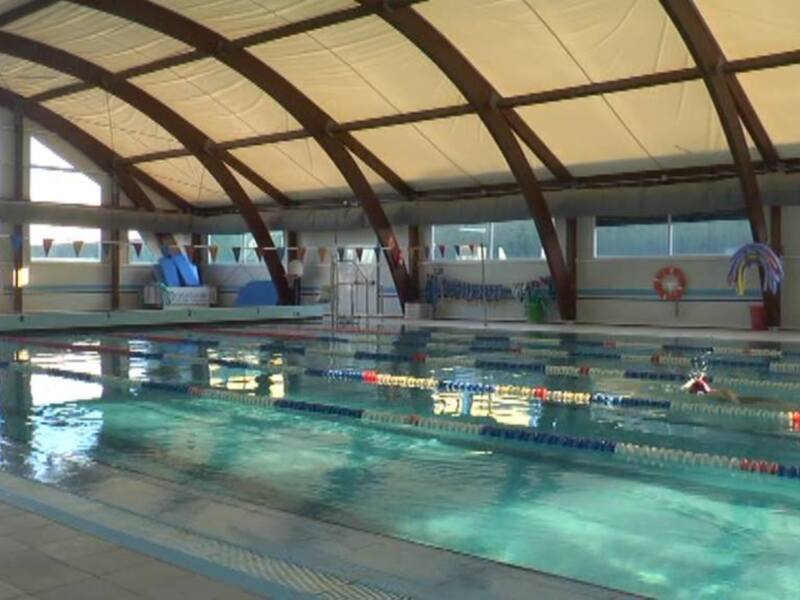Interior view of a spacious indoor swimming pool with a high arched roof and lane dividers.
