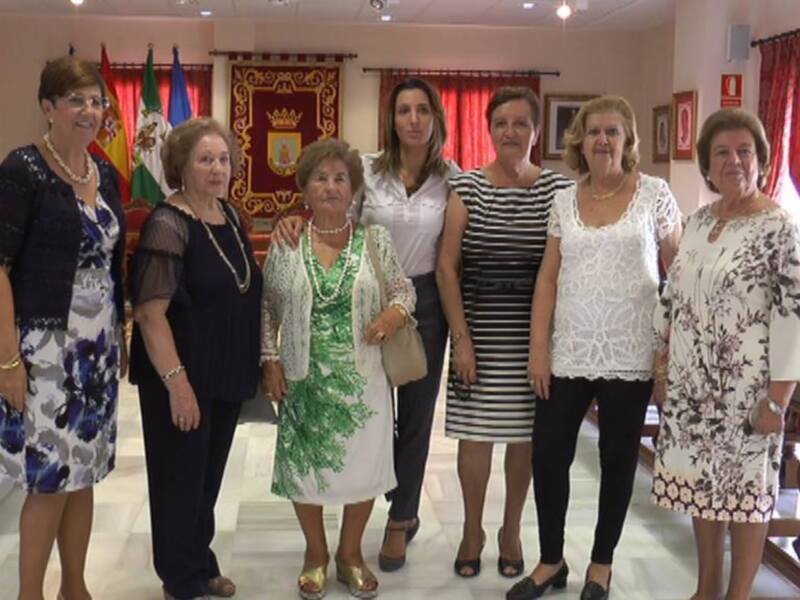 Señoras de diferentes edades y estilos vestidos, posando juntas en un ambiente decorado con banderas y una gran bandera.