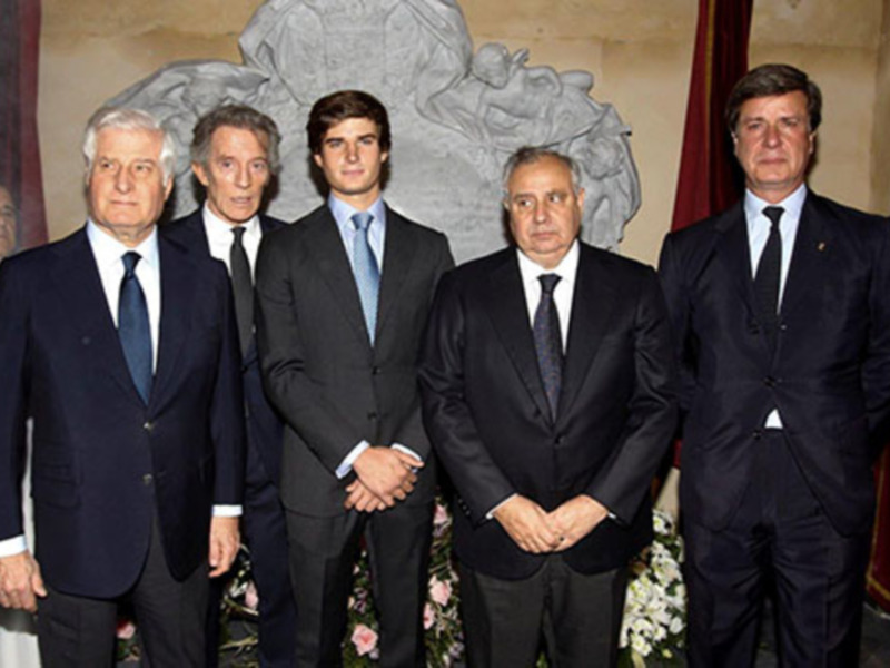 Ceremonia oficial con hombres en trajes formales frente a una estatua monumental.