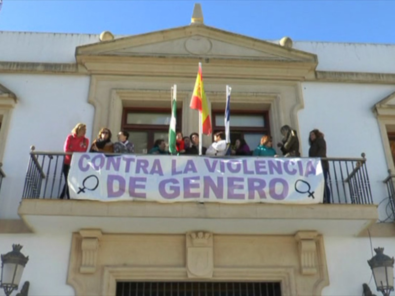 Manifestación contra la violencia de género en un balcón con banderas y pancarta.