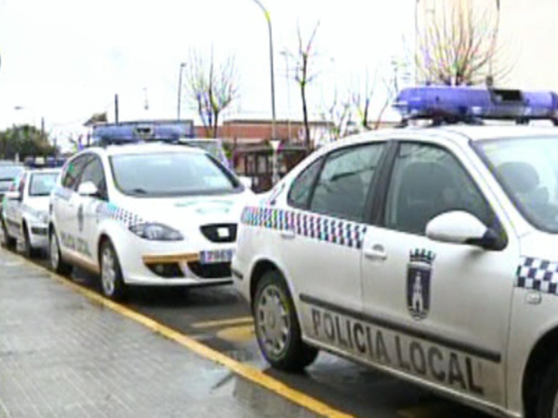 Varios coches de policía locales aparcados en una fila en una calle urbana.