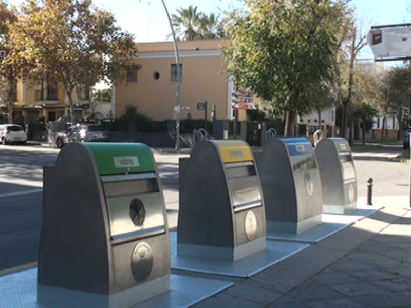 Estación de recarga de vehículos eléctricos en una calle con árboles y edificios al fondo.