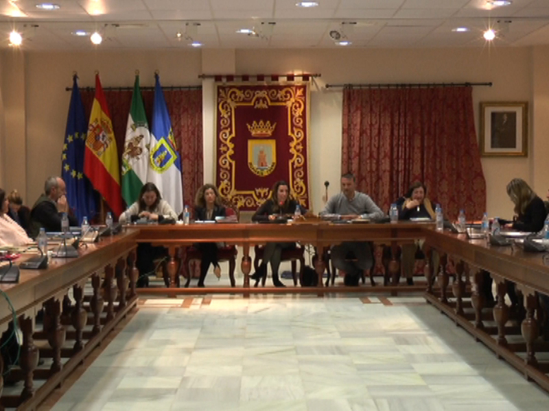 Sala de reuniones con una mesa larga en el centro, banderas y carteles decorativos en las paredes. Personas sentadas alrededor de la mesa, probablemente en una sesión de trabajo o conferencia. Ambiente formal y profesional.