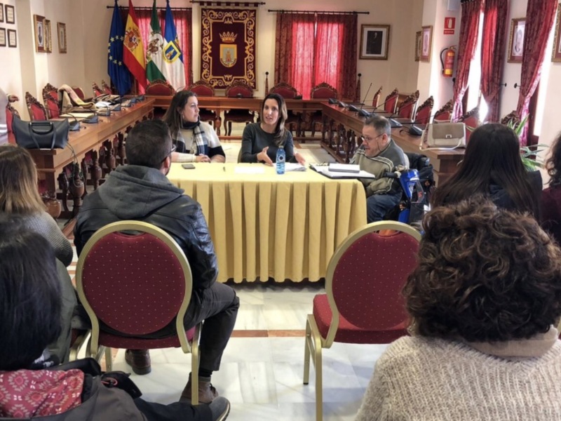 Sala de reuniones con mesas redondas, sillas rojas, banderas y un escudo en el fondo.