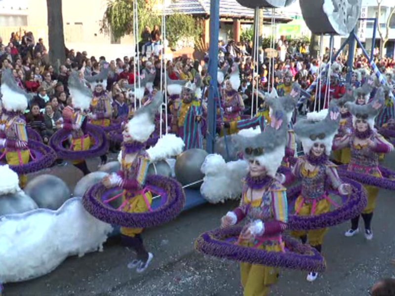 Desfile de carnaval con grupos de personas vestidas con trajes coloridos y sombreros festivos, desfilando frente a una multitud entusiasta.