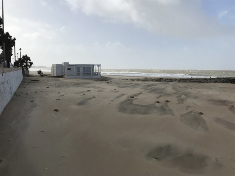 Casa blanca con terraza en la playa, arena y mar en el fondo.