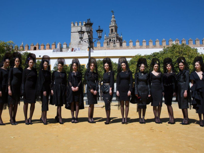 Un grupo de mujeres vestidas de negro posa frente a un edificio histórico bajo un cielo azul claro.