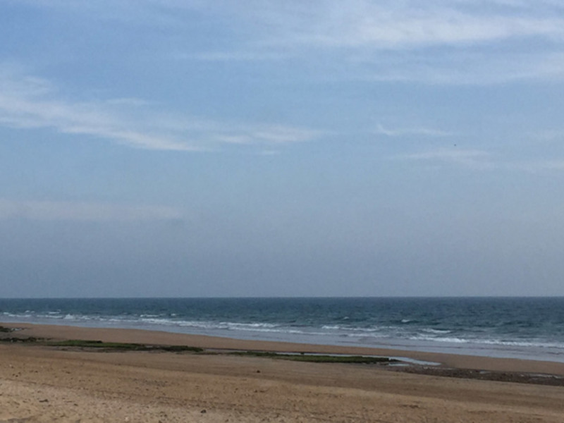 Playa desierta con arena dorada y mar azul profundo. El cielo está claro, con algunas nubes dispersas. La imagen captura la tranquilidad y belleza de un día soleado en la costa.