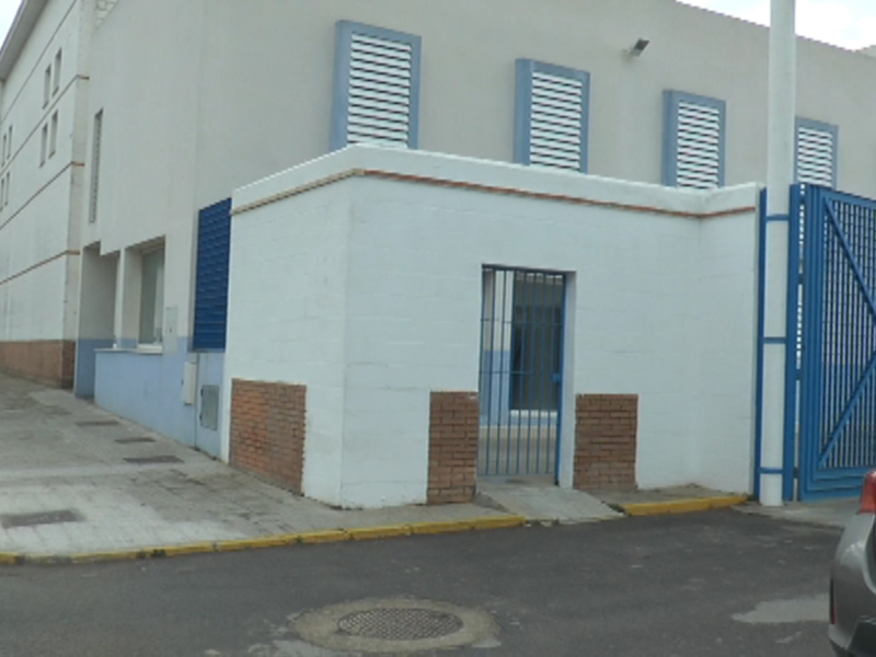Edificio blanco con azulejos y puerta metálica, cerca de una calle con señales de tráfico.