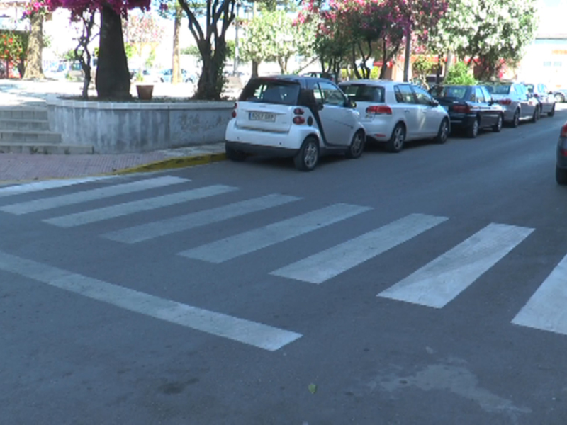 Calle con línea de cebra, coches estacionados y árboles en flor.