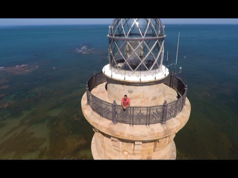 Un hombre se sienta en el borde del faro, disfrutando de la vista panorámica sobre el mar y las islas.