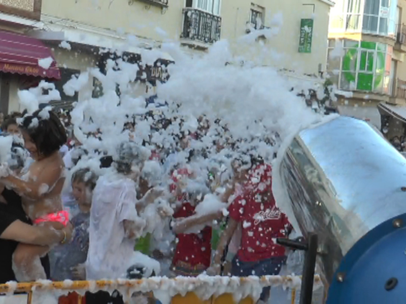 Una celebración festiva con mucha espuma en el aire y personas disfrutando de la diversión.