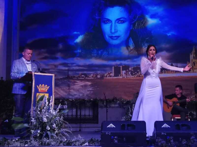 Concierto de música en vivo con una cantante en escenario, fondo de pantalla con una imagen de una mujer y una vista de la ciudad.