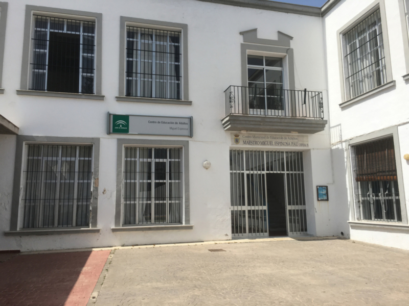 Centro de Educación Infantil. Edificio blanco con ventanas de barra y entrada principal. Piso superior con balcón. Sello del Ayuntamiento en la fachada.