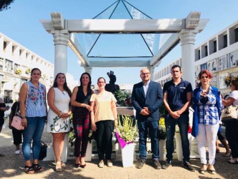 Grupo de personas posando frente a un arco clásico en un entorno urbano soleado.