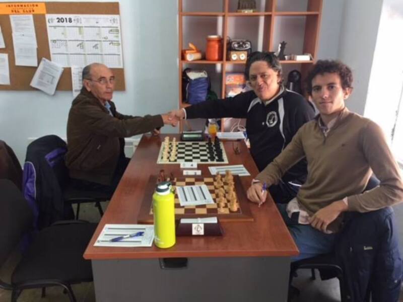 Tres personas se reúnen en una sala de ajedrez, celebrando un acuerdo con un apretón de manos.