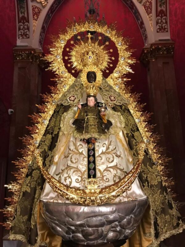 Imagen de la Virgen María en una iglesia, vestida con trajes tradicionales y coronada con una elegante corona dorada.