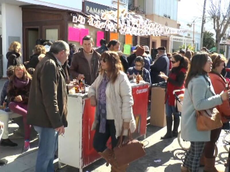 Una multitud de personas se reúne en un evento al aire libre, con stands de comida y decoraciones festivas en el fondo.