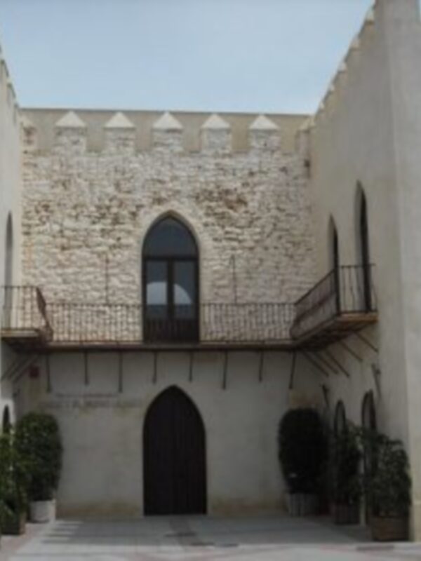 Una estructura histórica con torres y balcones, posiblemente parte de un castillo o palacio medieval. La arquitectura es típica del siglo XVII, con muros de piedra y detalles en ladrillo. En el frente hay plantas verdes, lo que indica un entorno cuidado y bien mantenido. La estructura parece estar en buen estado, sugiriendo que es un lugar de interés histórico o turístico.