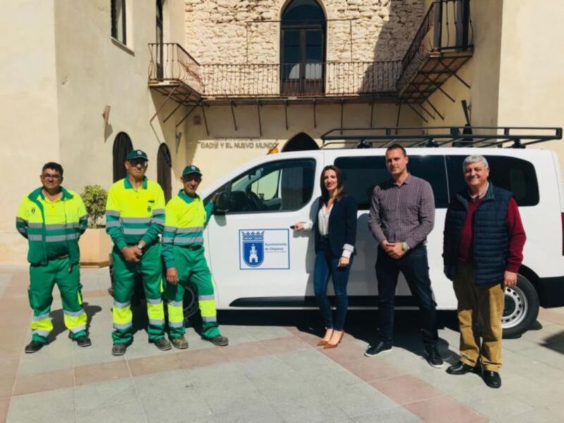Equipo de trabajadores ambientales en uniforme verde y amarillo frente a una furgoneta blanca con logotipo de la municipalidad. En el fondo, edificio histórico con balcones y ventanas.