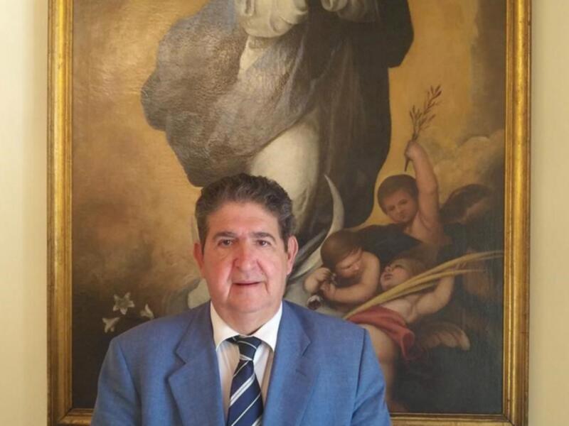 Hombre en traje frente a un lienzo con figuras angelicales.