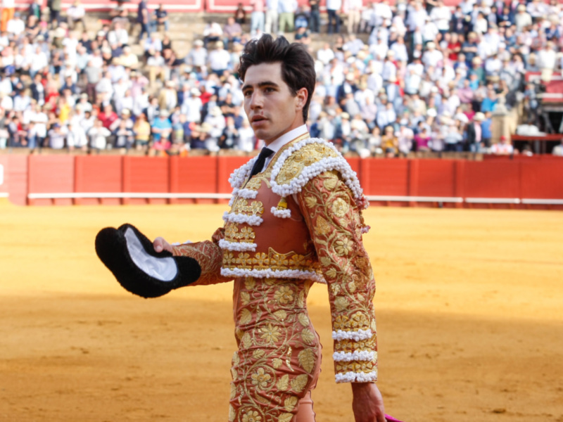 Matador en traje de luces, presentando el sombrero en el ruedo durante una corrida de toros.
