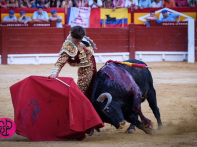 Un torero lidiando un toro en una corrida de toros, con el público en el fondo.