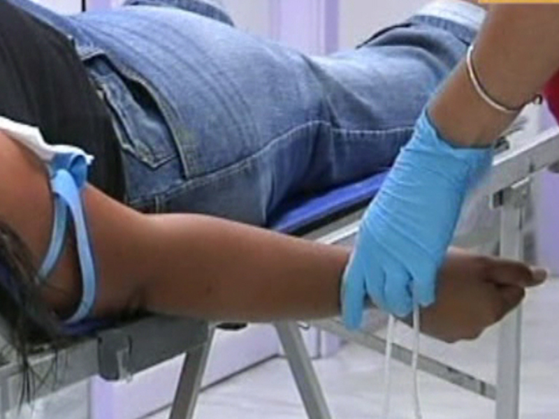 Persona en una camilla de hospital con un brazo en una muñequera azul, mientras un profesional de la salud ajusta el dispositivo en el brazo.