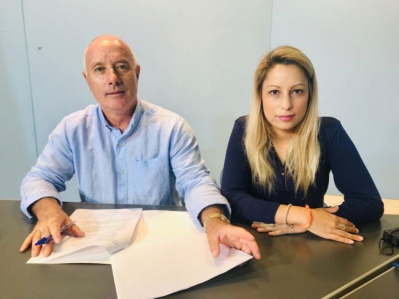 Dos personas sentadas frente a una mesa, uno con un papel y la otra con un teléfono.