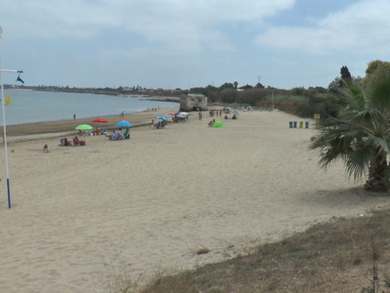 Playa con personas sentadas bajo sombrillas de colores, arena blanca y agua azul.