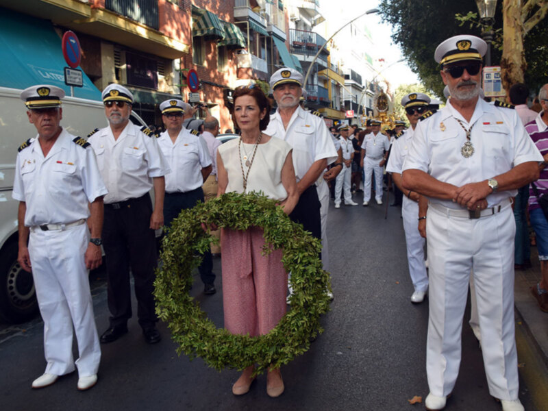 Desfile con uniformes militares y una mujer con corona de laurel en un entorno urbano.