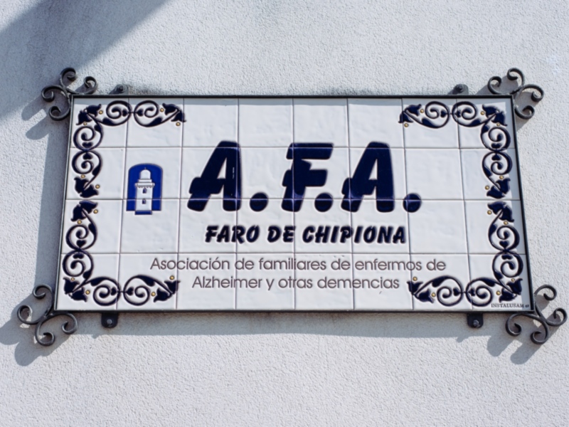 Un cartel de cerámica con un diseño azul y blanco que muestra una linterna y el nombre "A.F.A." junto con la frase "Faro de Chipiona".